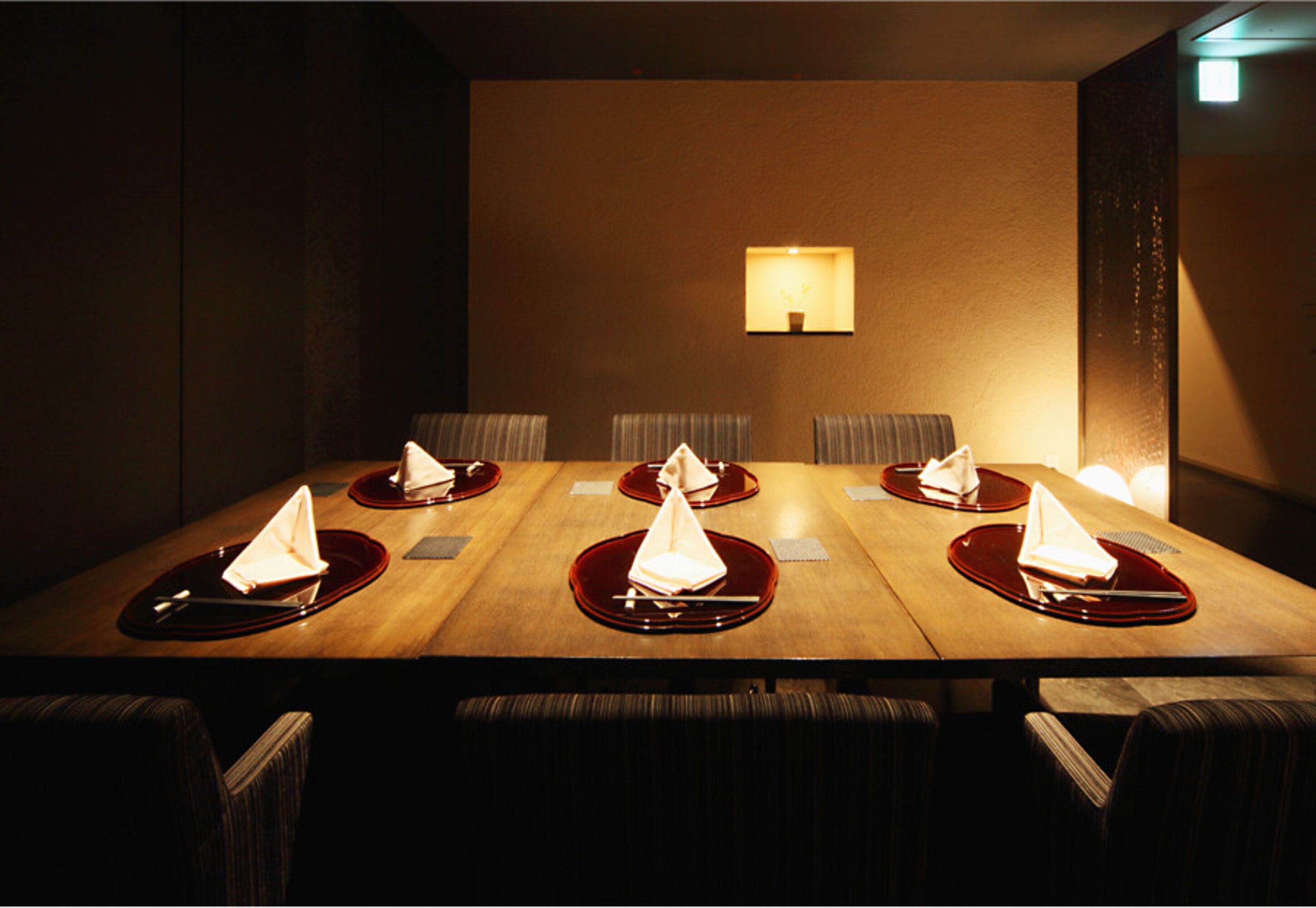 A conference room with a long table, six chairs, and a wall-mounted lamp.