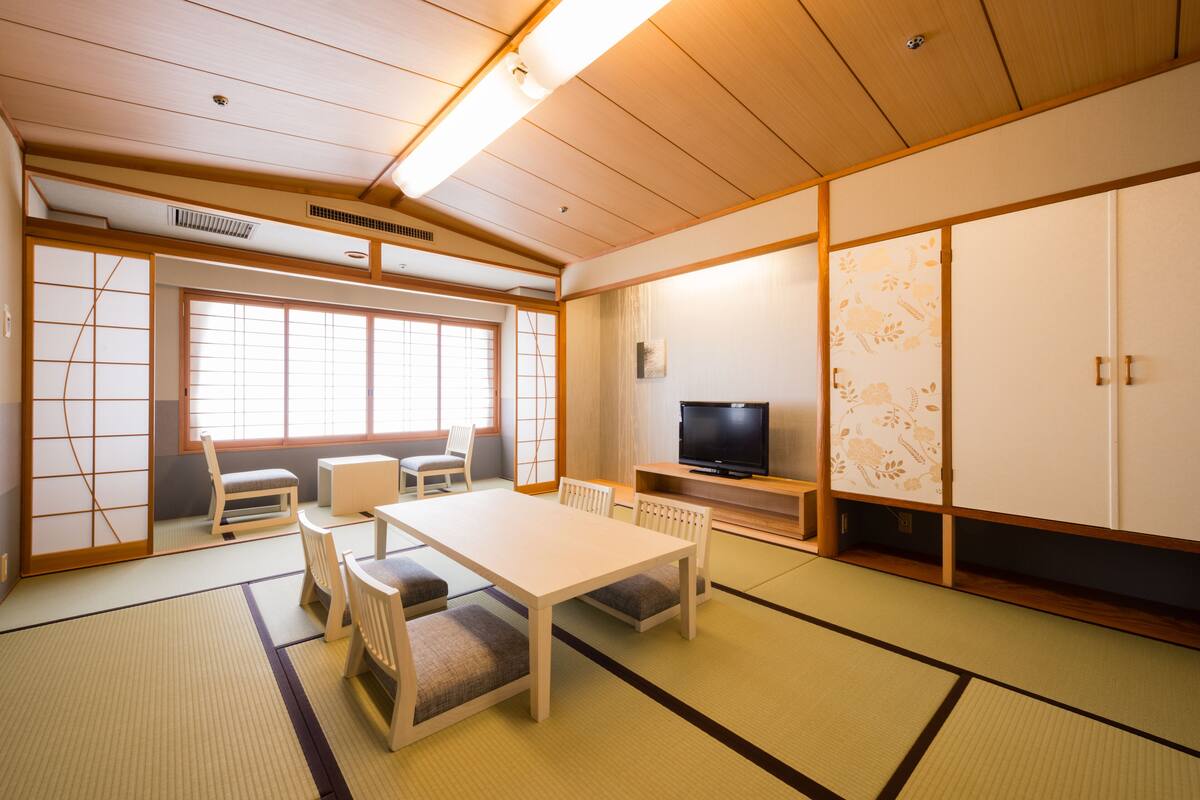 A traditional Japanese room with tatami flooring, a low table with cushions, a television, and sliding doors.