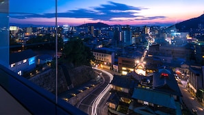 A cityscape at dusk with illuminated buildings and a winding road. - Chaharu (Matsuyama)