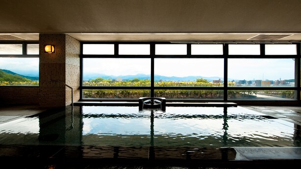 An indoor swimming pool with a view of mountains and cityscape through large windows. - Chaharu (Matsuyama)