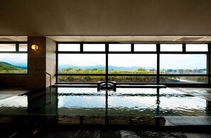 An indoor swimming pool with a view of mountains and cityscape through large windows. - Chaharu (Matsuyama)