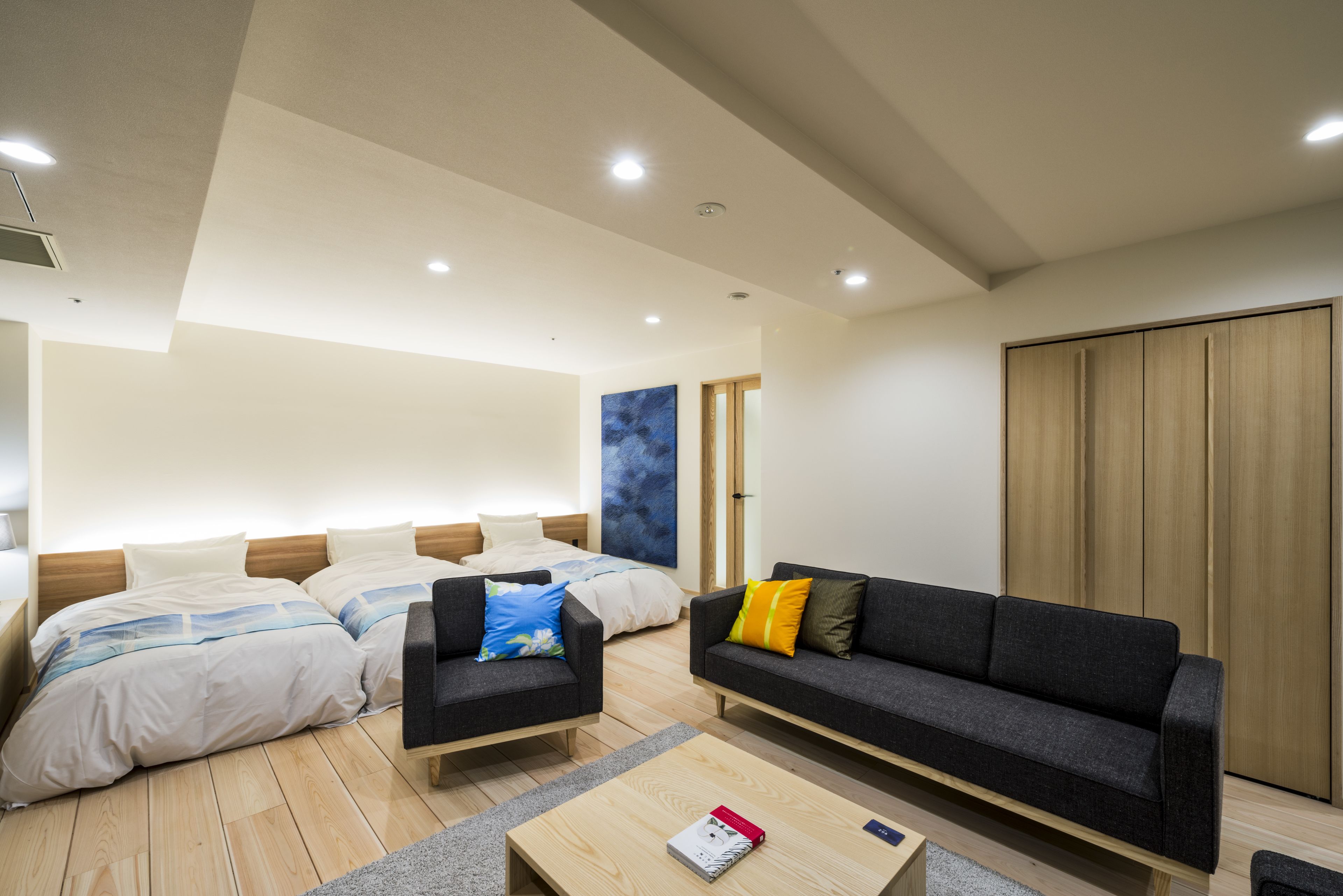 A modern hotel room with a large bed, two sofas, a wooden coffee table, and a wardrobe.