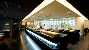 A modern buffet setup with a central serving area, multiple food stations, and a long counter with plates. - Chaharu (Matsuyama)