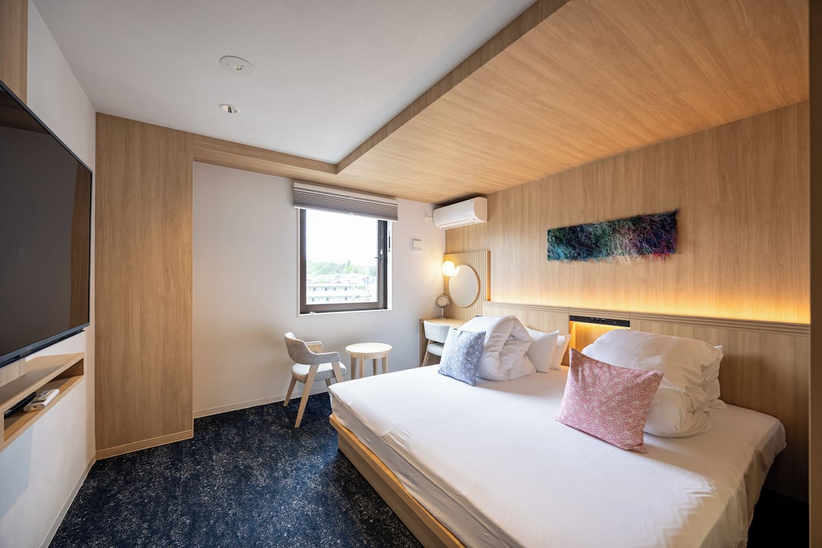 A hotel room with a bed, a desk, a chair, a TV, and a window.