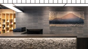 A reception area with a stone-textured counter, a wooden shelf with wine bottles, and a wall-mounted artwork depicting a mountain. - HOTEL FUJi TORiiGATE (Fujiyoshida)