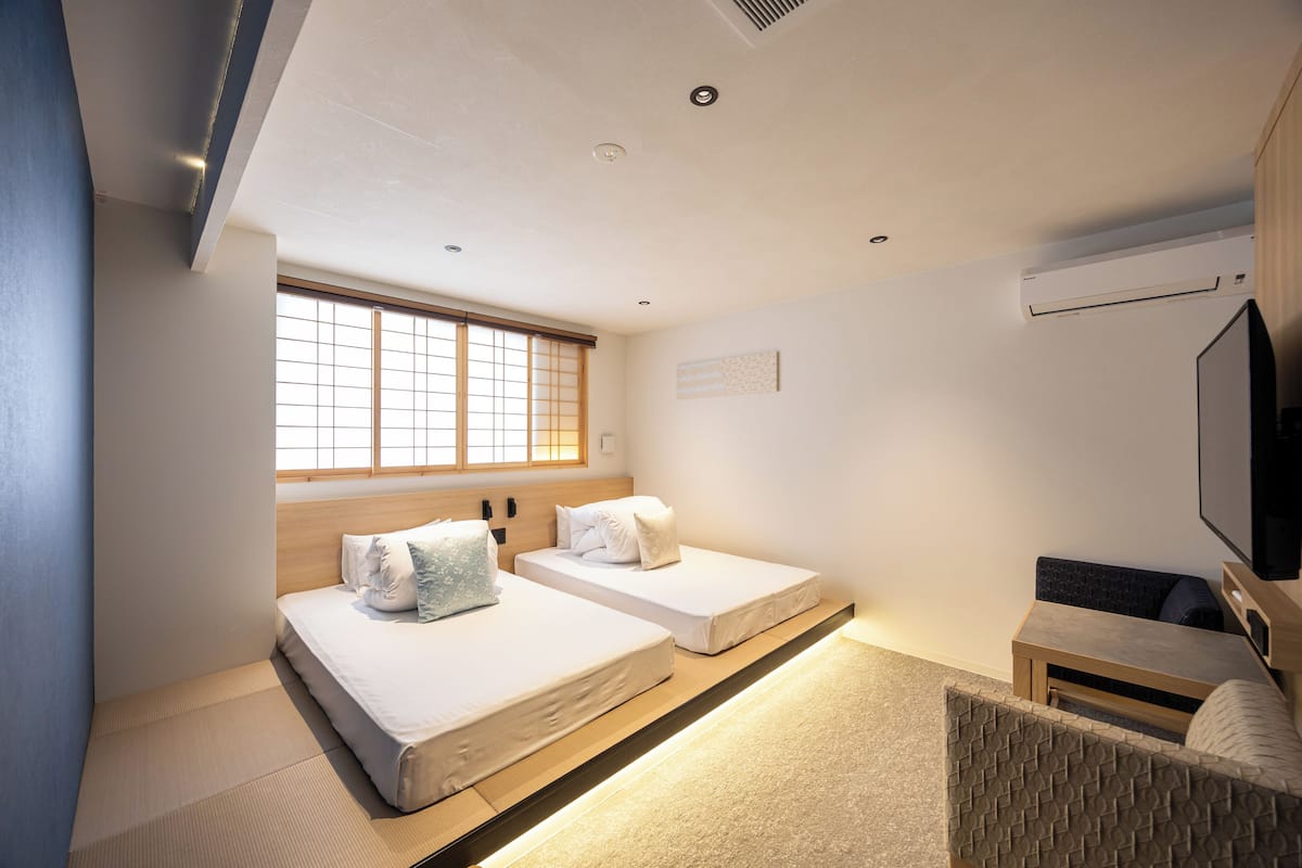 A hotel room with two beds, a TV, and a window with blinds.