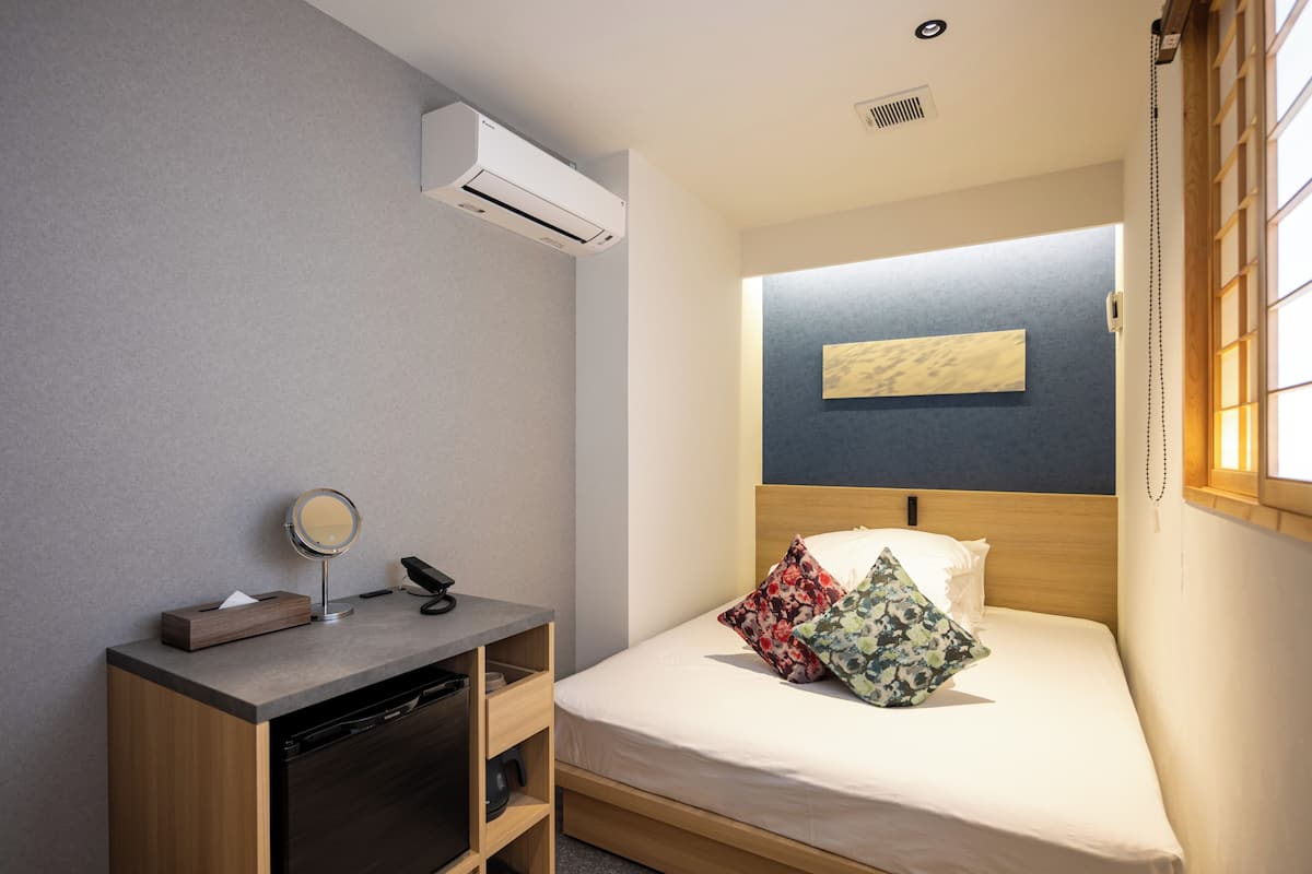 A compact room with a bed, a desk with a mirror, and an air conditioning unit.
