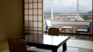 A traditional Japanese room with tatami flooring, a low table, and chairs. A large window offers a view of a mountainous landscape.