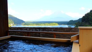 A hot spring bath with a wooden railing, a view of a lake, and a mountain in the distance.