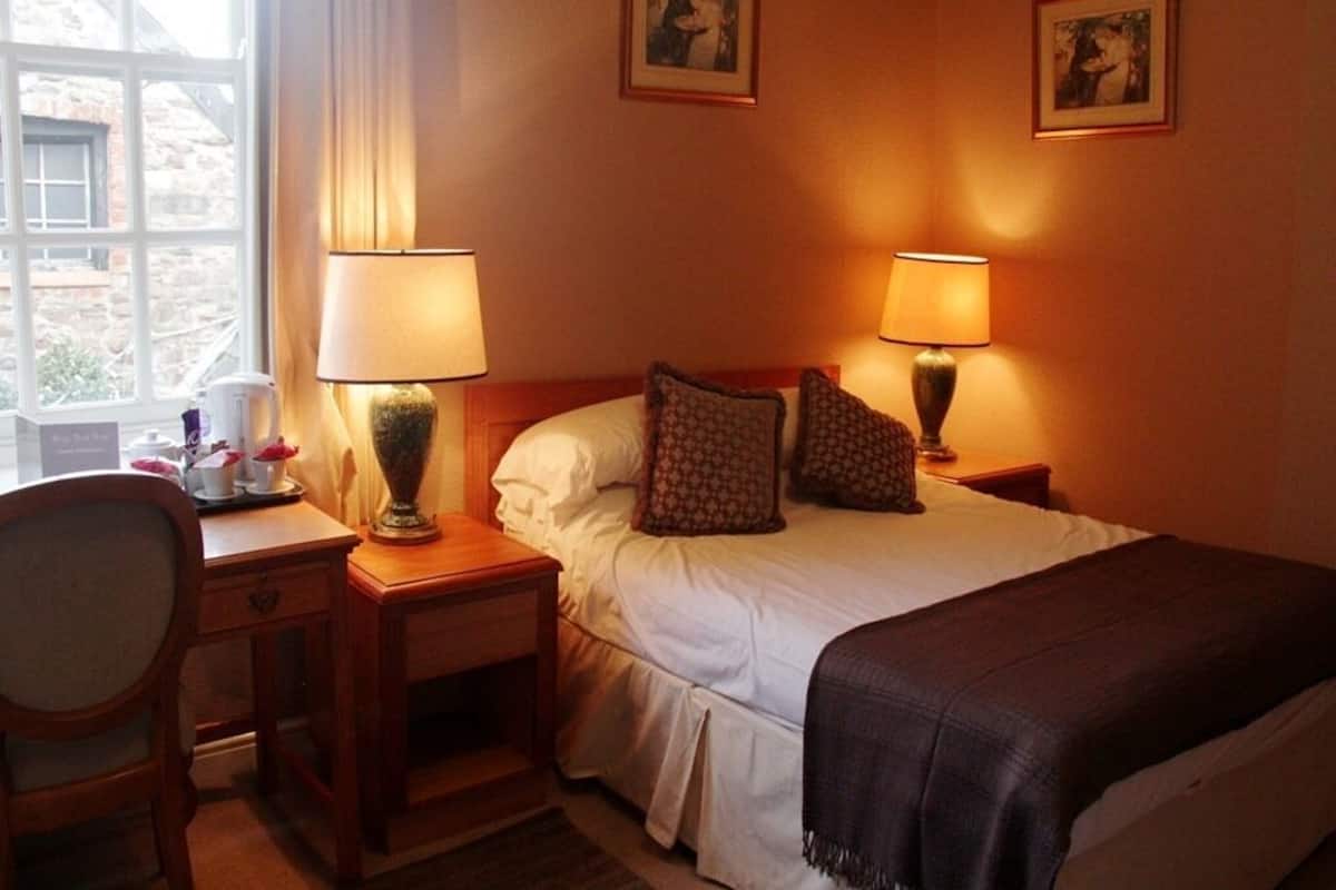 Habitación de hotel con una cama, dos lámparas de noche, un escritorio con una silla y dos cuadros en la pared.