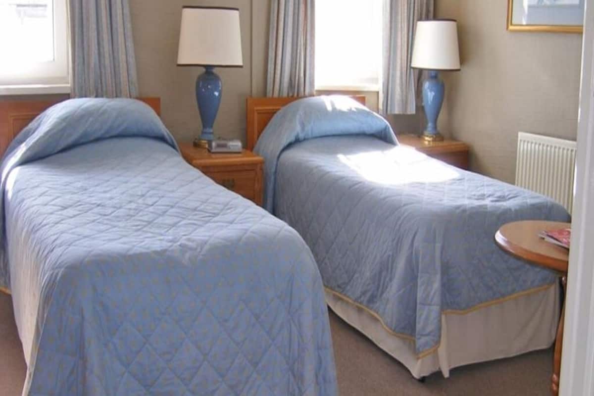 Habitación de hotel con dos camas, cada una con colcha azul acolchada, cabeceros de madera y lámparas de noche.