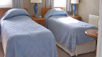 Habitación de hotel con dos camas, cada una con colcha azul acolchada, cabeceros de madera y lámparas de noche.