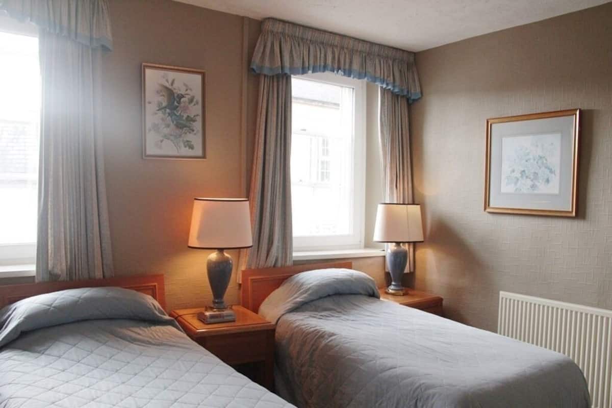 Habitación de hotel con dos camas, una ventana con cortinas, un radiador y dos lámparas fijadas a la pared.