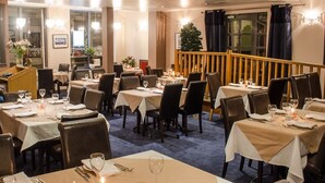Un restaurant avec de nombreuses tables dressées pour le service, agrémentées de nappes blanches et de centres de table à bougies.
