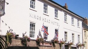Un bâtiment blanc portant l’enseigne « Kings Head Hotel » et sur lequel flottent de nombreux drapeaux.