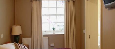 A hotel room with a bed, a bedside lamp, a TV, and a window with curtains.