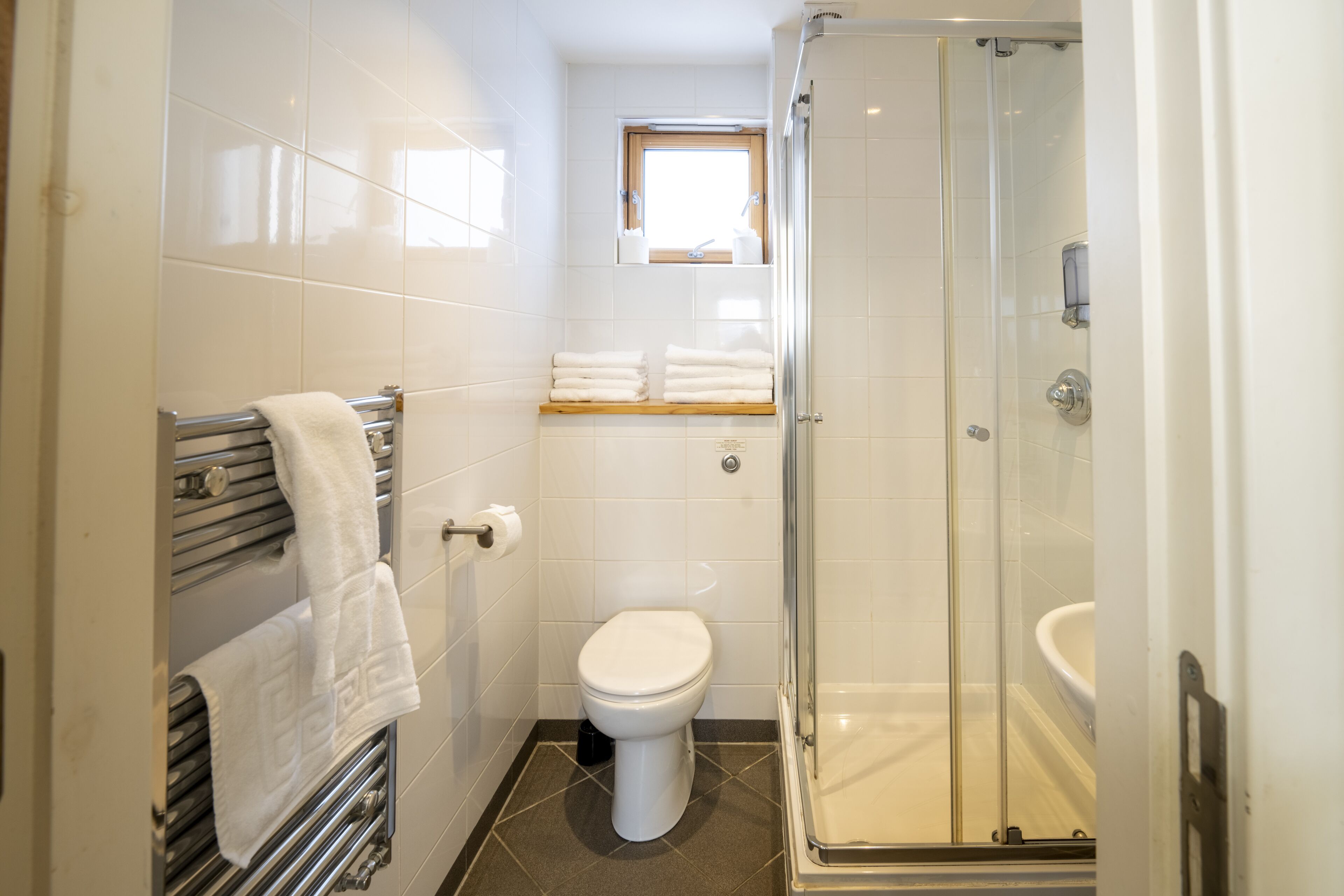 A bathroom with a glass-enclosed shower, a toilet, and a towel rack with folded towels.