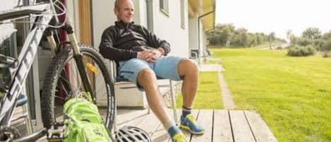 A person sitting on a wooden deck with a bicycle and a green bag beside them.
