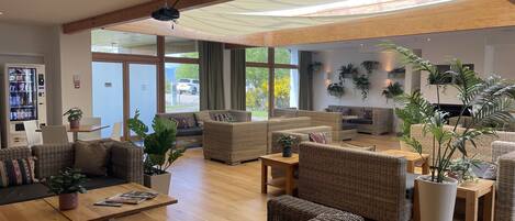 Amplia sala de estar con mobiliario de mimbre, una cafetera y ventanas grandes que ofrecen vistas al exterior.