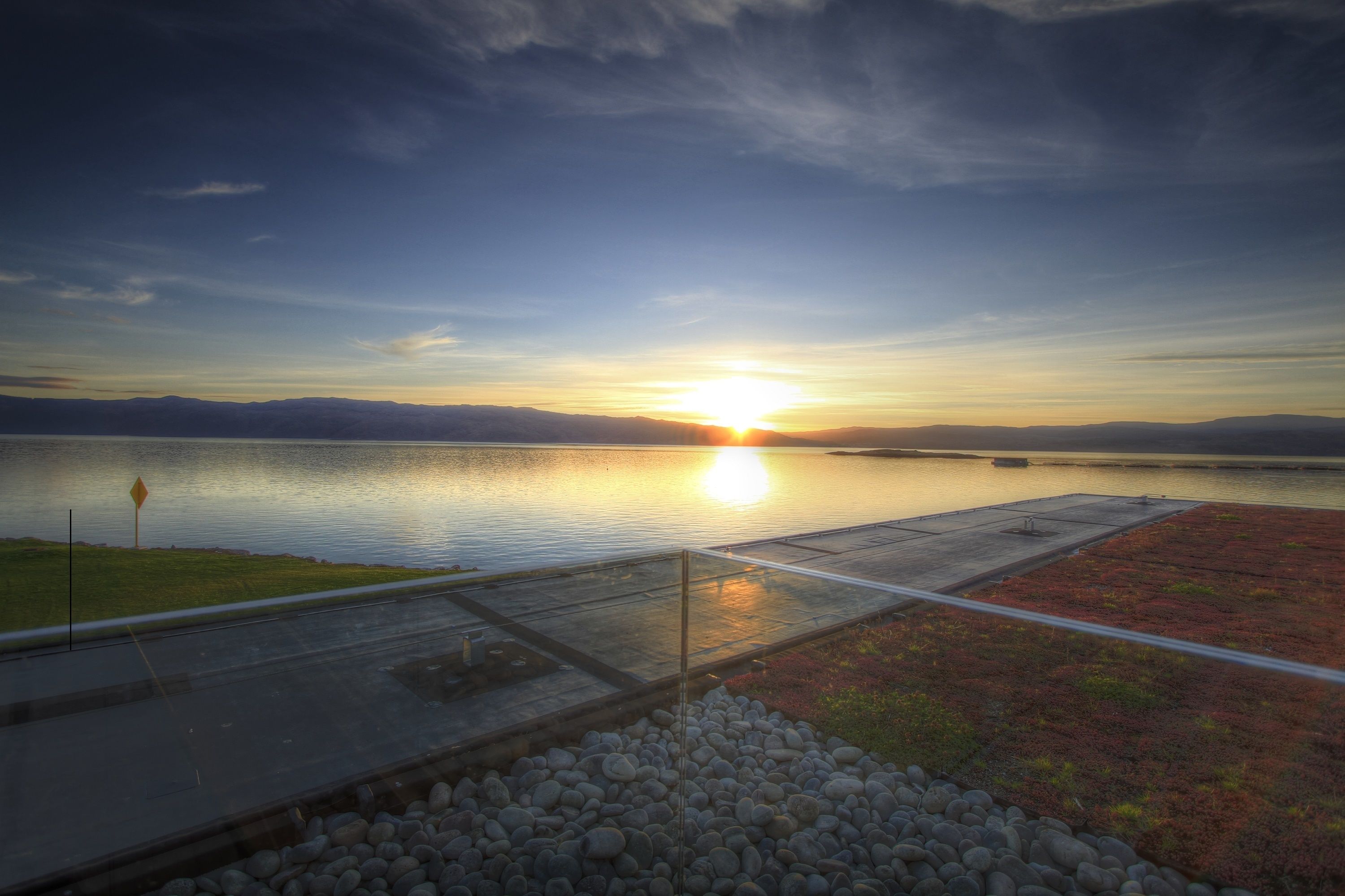 Un atardecer sobre un lago tranquilo con un muelle y una orilla rocosa.