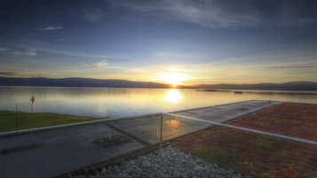 Un atardecer sobre un lago tranquilo con un muelle y una orilla rocosa.