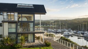 A modern two-story building with a balcony overlooking a marina with boats.