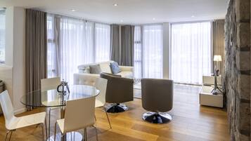 A modern living room with a glass dining table, white and gray chairs, a gray sofa, and a stone accent wall.