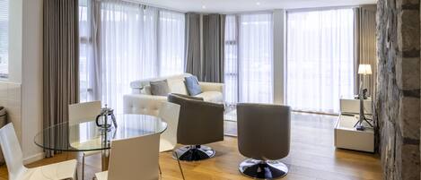 A modern living room with a glass dining table, white and gray chairs, a gray sofa, and a stone accent wall.