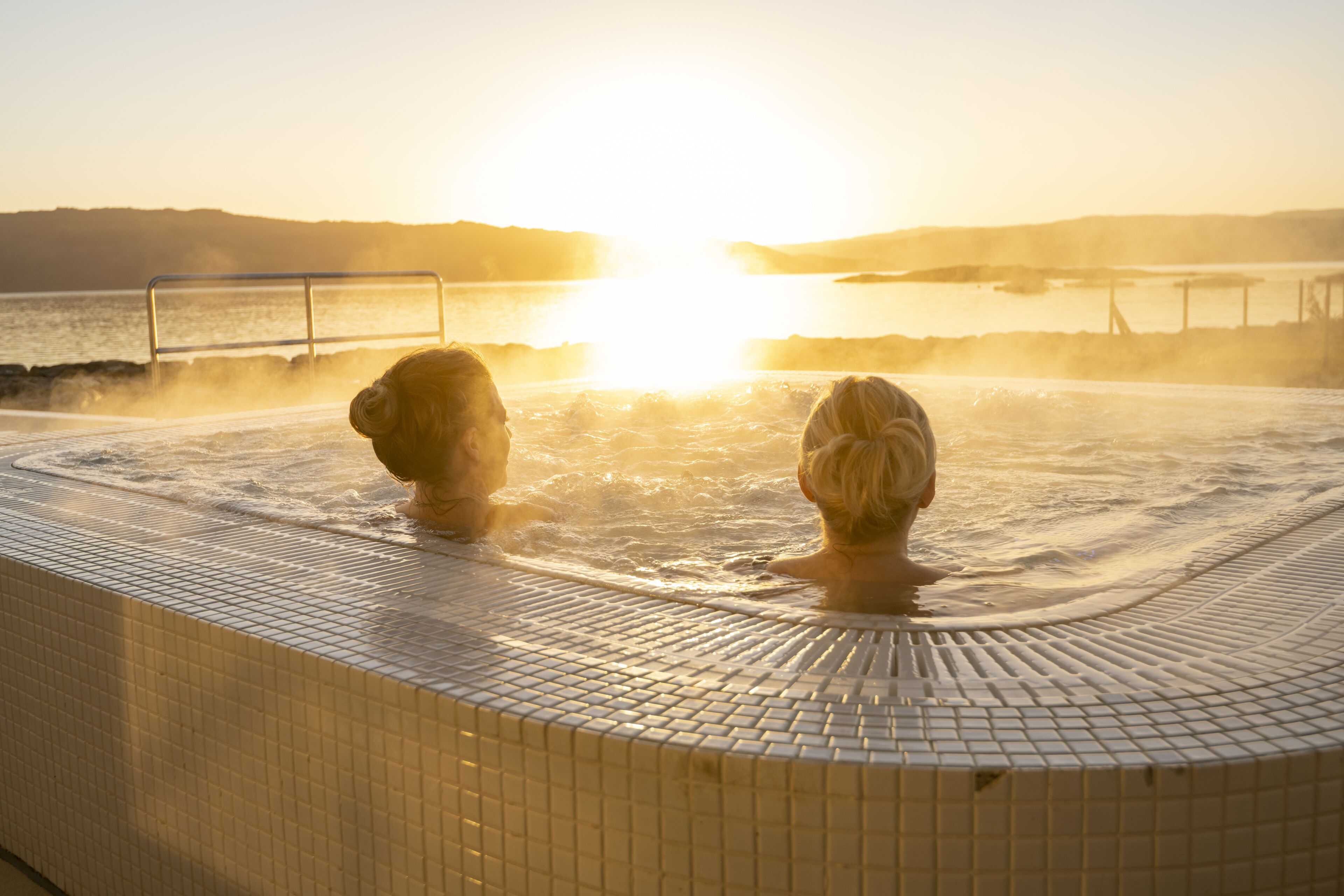 A hot tub with a tiled edge and a view of the sunset over water.