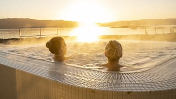 A hot tub with a tiled edge and a view of the sunset over water.