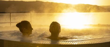 Two people in a hot tub with a sunset in the background.