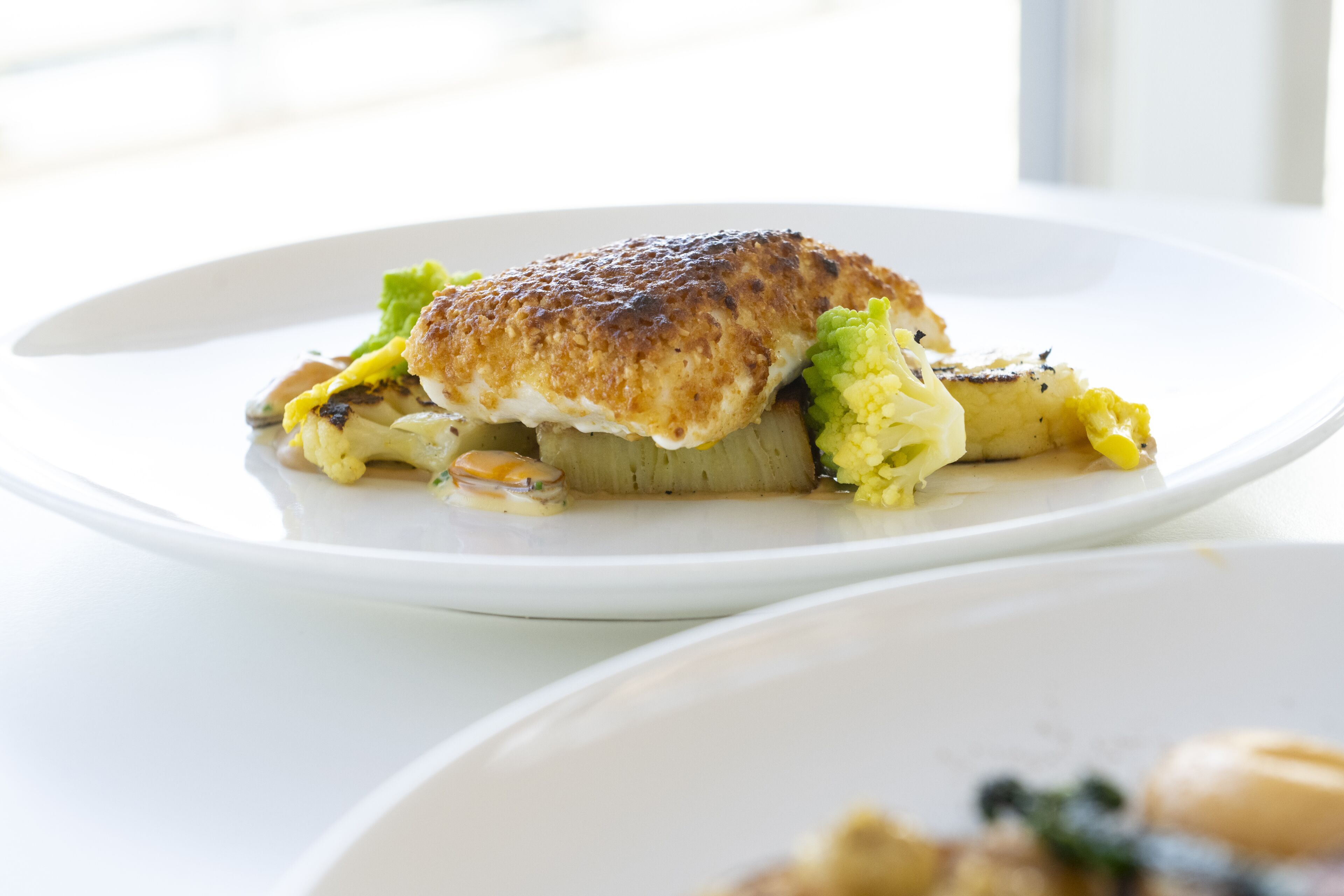 Un piatto con un trancio di pesce alla griglia, verdure verdi e una fetta di pane.