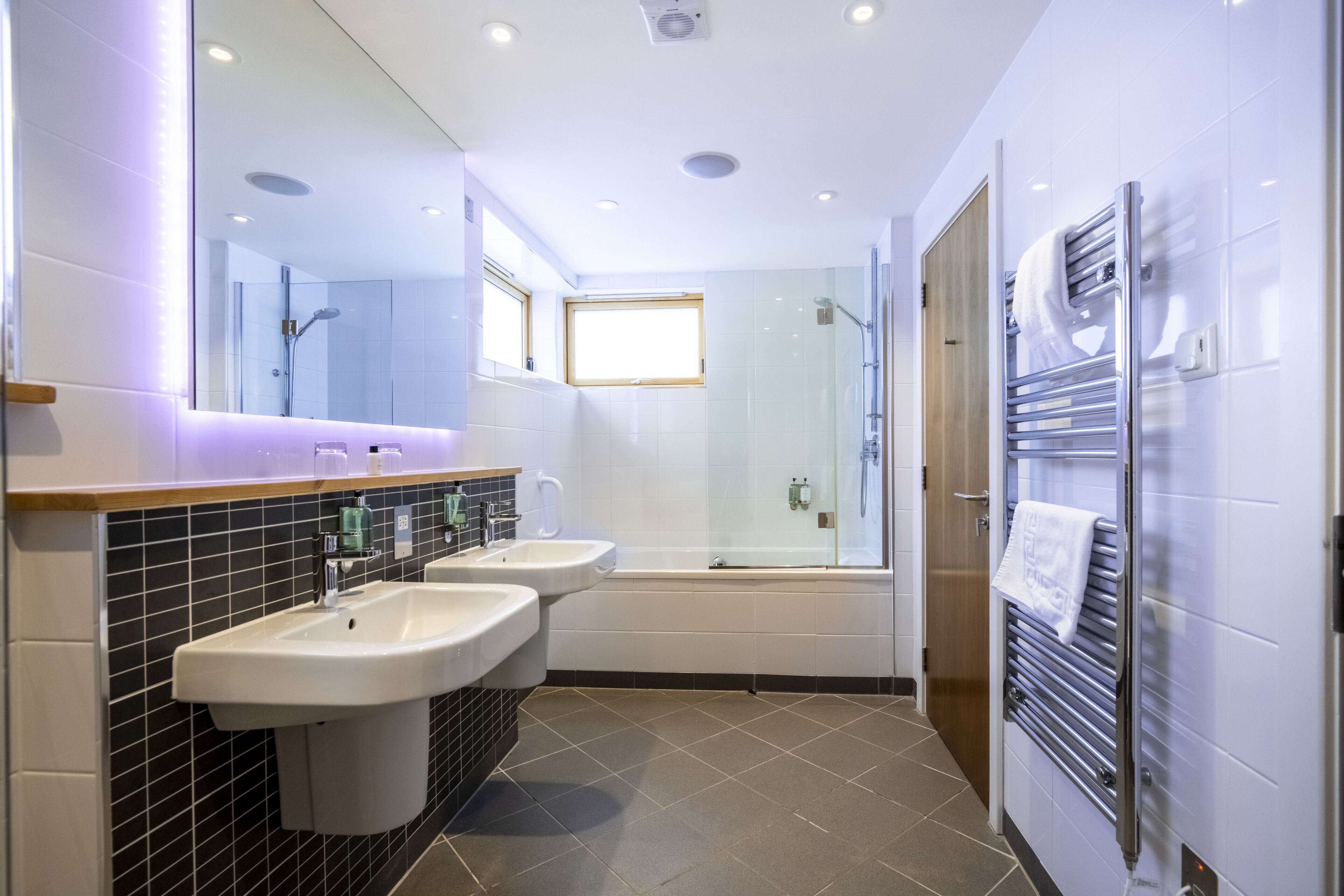 Un baño moderno con dos lavamanos, un espejo grande, cabina de ducha de vidrio y un perchero para toallas.