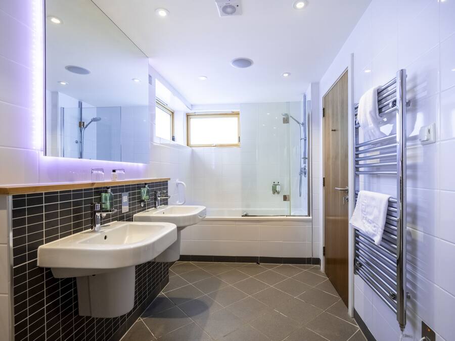 Un baño moderno con dos lavamanos, un espejo grande, cabina de ducha de vidrio y un perchero para toallas.