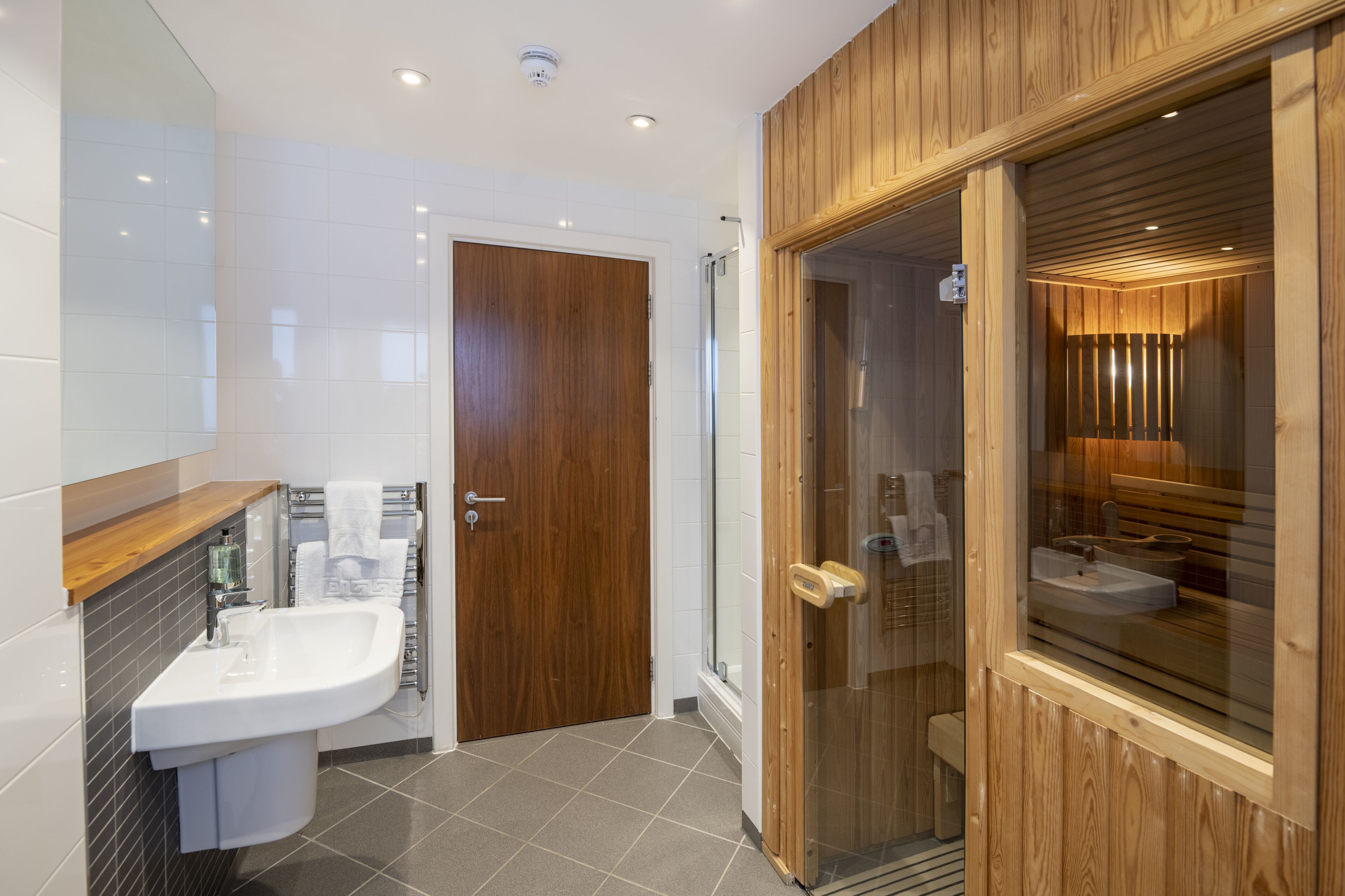 A modern bathroom with a wooden vanity, a glass-enclosed shower, and a white sink.
