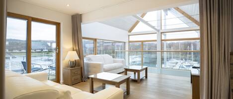 A spacious living room with a large window, a sofa, a coffee table, and a lamp.