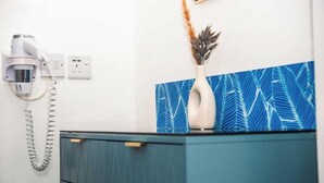 A bathroom with a blue cabinet, a white vase with a pineapple, and a hairdryer on a wall-mounted outlet. - Elgano (Cardiff)