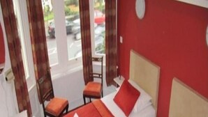 A hotel room with four single beds, each with a red bedspread and white pillows. There is a small table and a chair in the corner. - Elgano (Cardiff)