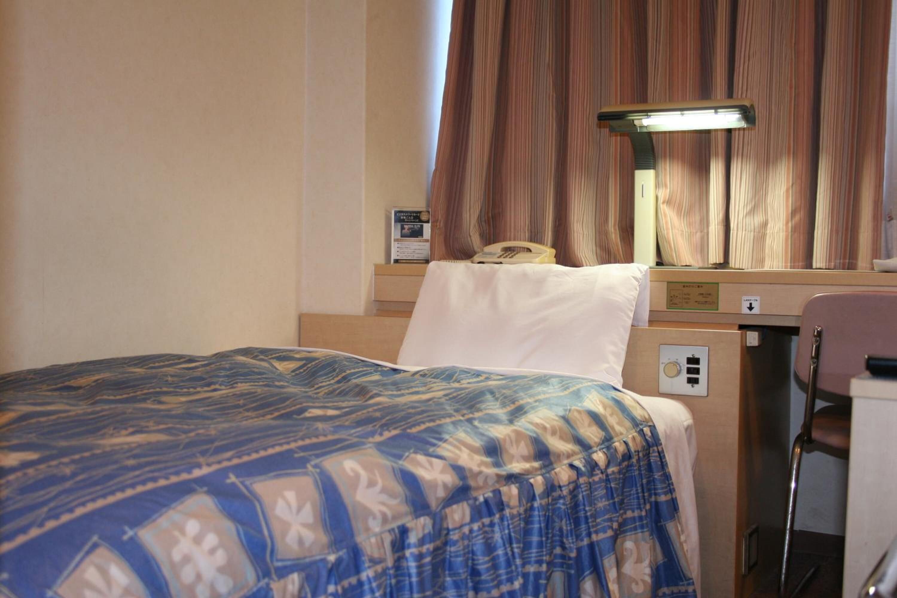 Habitación de hotel con cama, escritorio, teléfono, lámpara y cortinas.