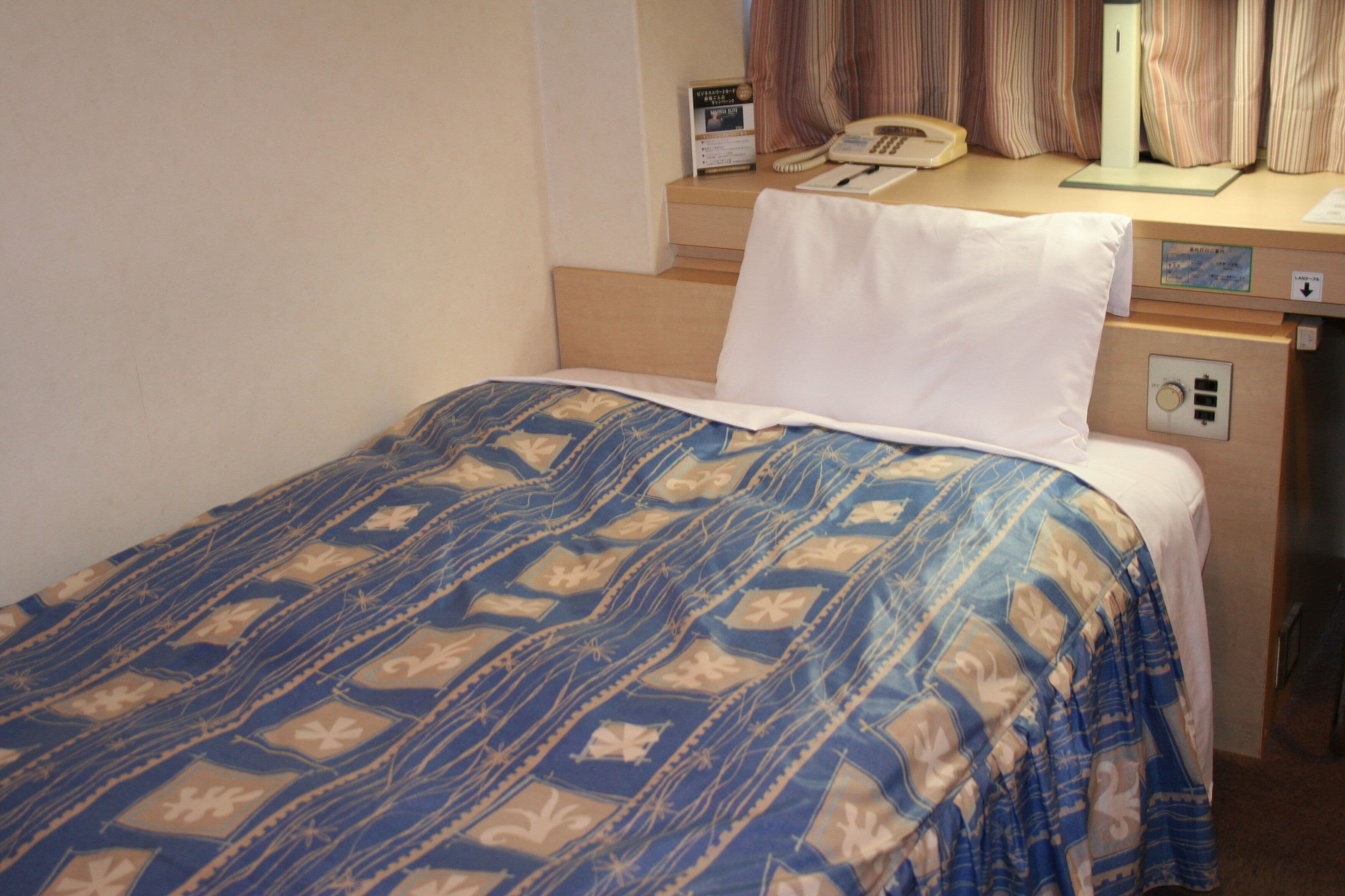 A hotel room with a bed, a desk, a telephone, and a nightstand.