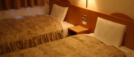 Deux lits côte à côte dans une chambre d’hôtel, avec des têtes de lit, une table de chevet et une lampe fixée au mur.