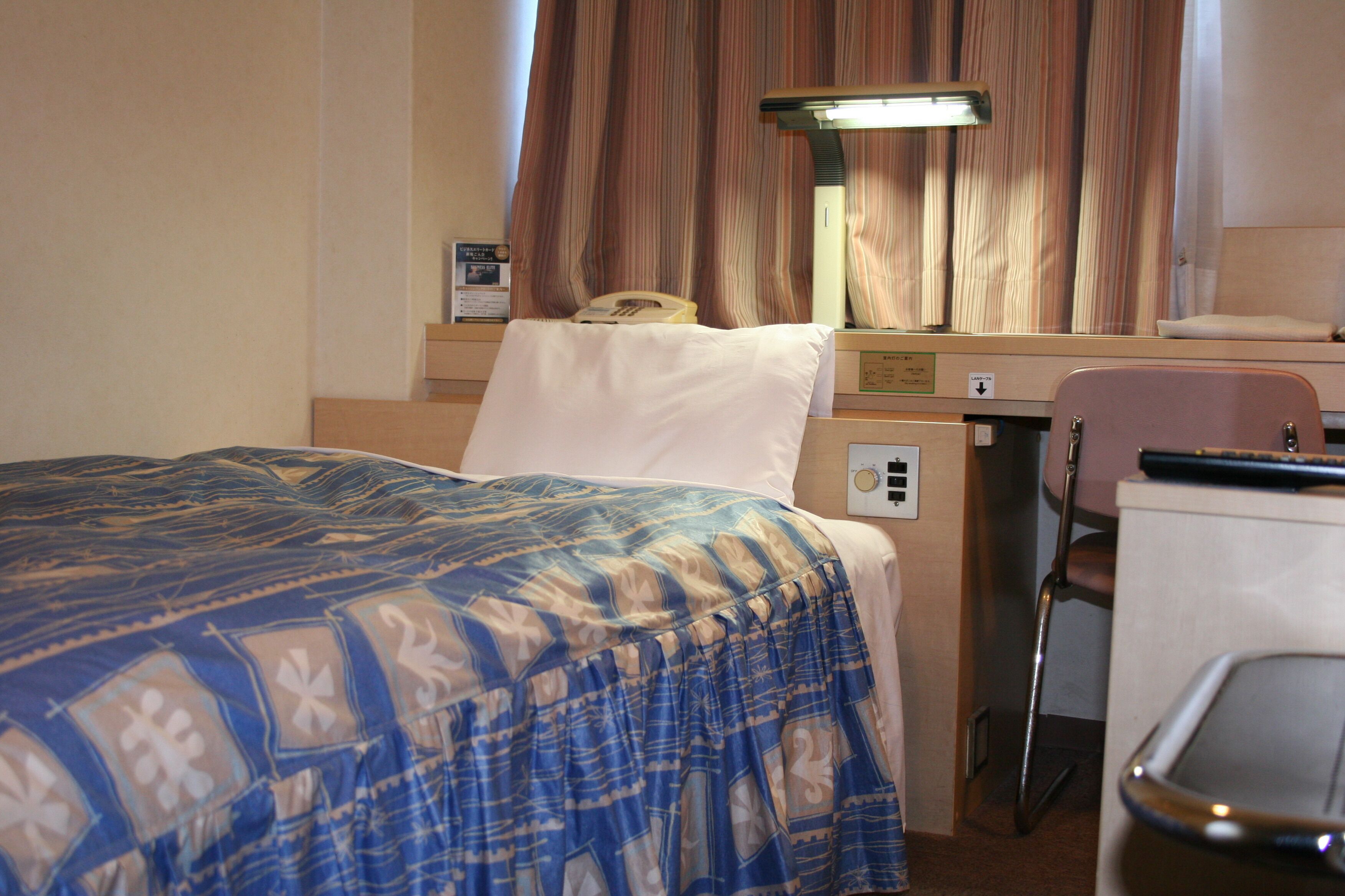 Una habitación de hotel con cama, escritorio, silla, lámpara y teléfono.