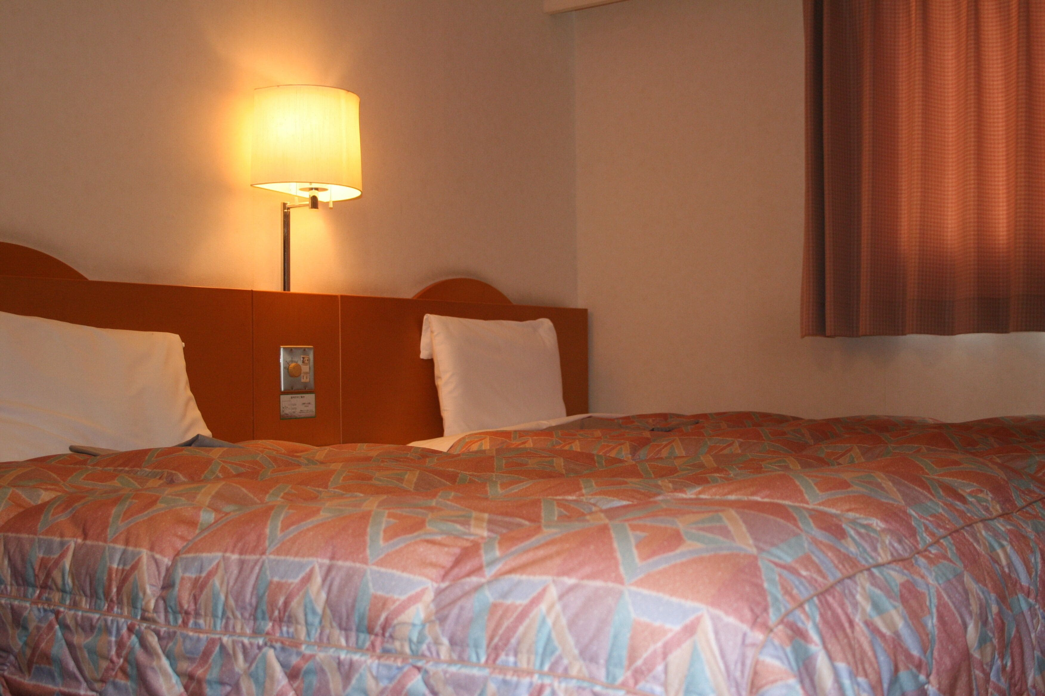 A hotel room with a large bed, a nightstand, a lamp, and a window with curtains.