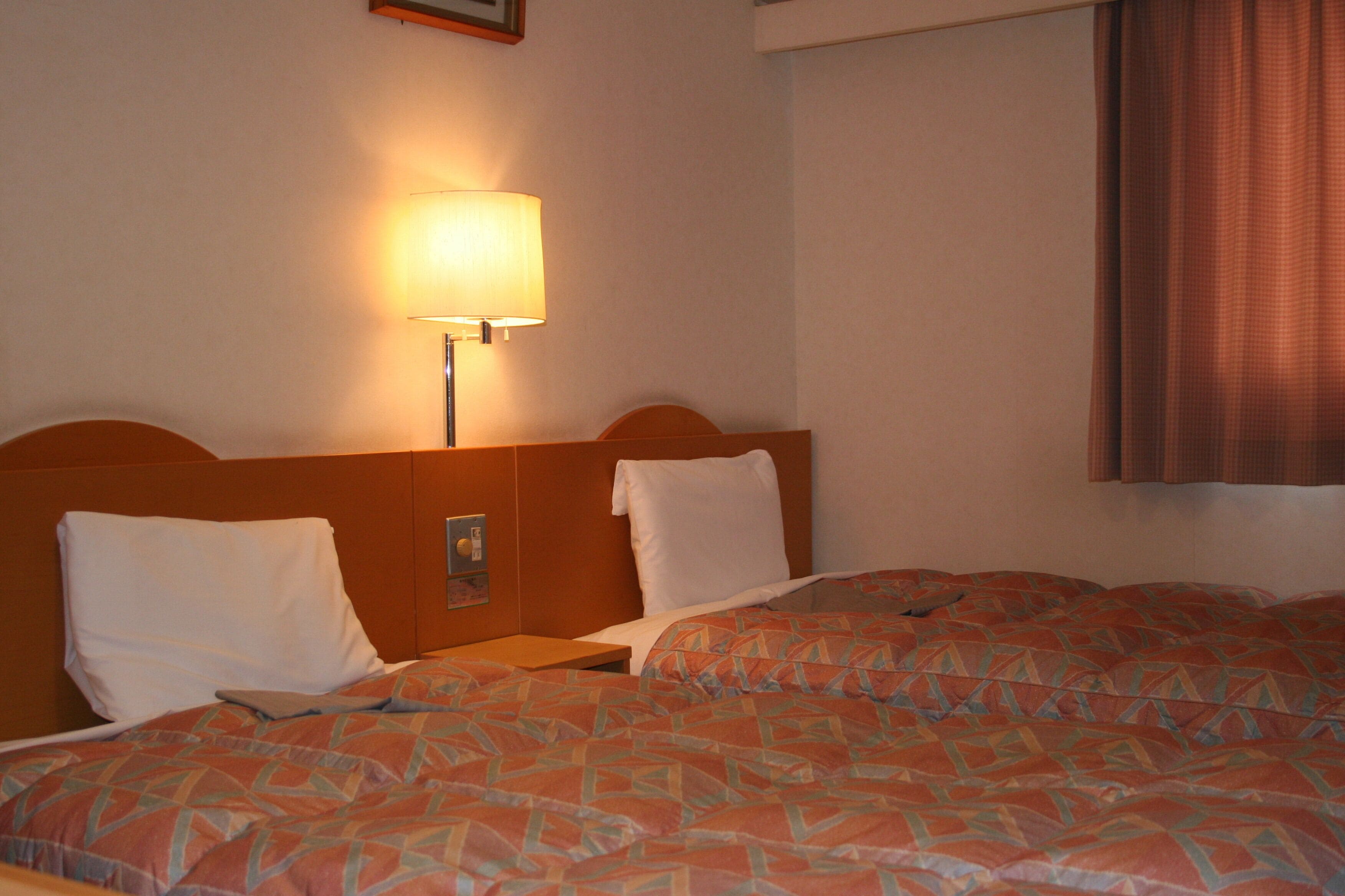 A hotel room with two beds, a nightstand, a lamp, and a window with curtains.