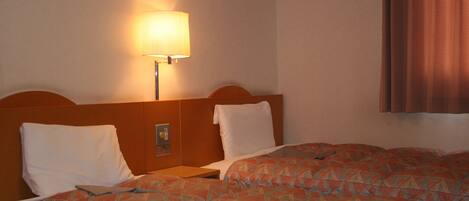 Habitación de hotel con dos camas, una mesita de noche, una lámpara y una ventana con cortinas.