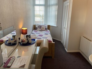 A hotel room with a bed, a desk with a lamp, a tray with breakfast items, a remote control, and a sign indicating no clock. - Austins Self Service Guest House (Cardiff)