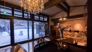 A cozy interior with a large window, wooden beams, a chandelier, and a sofa with cushions. - Natsuse Onsen Miyakowasure (Senboku)