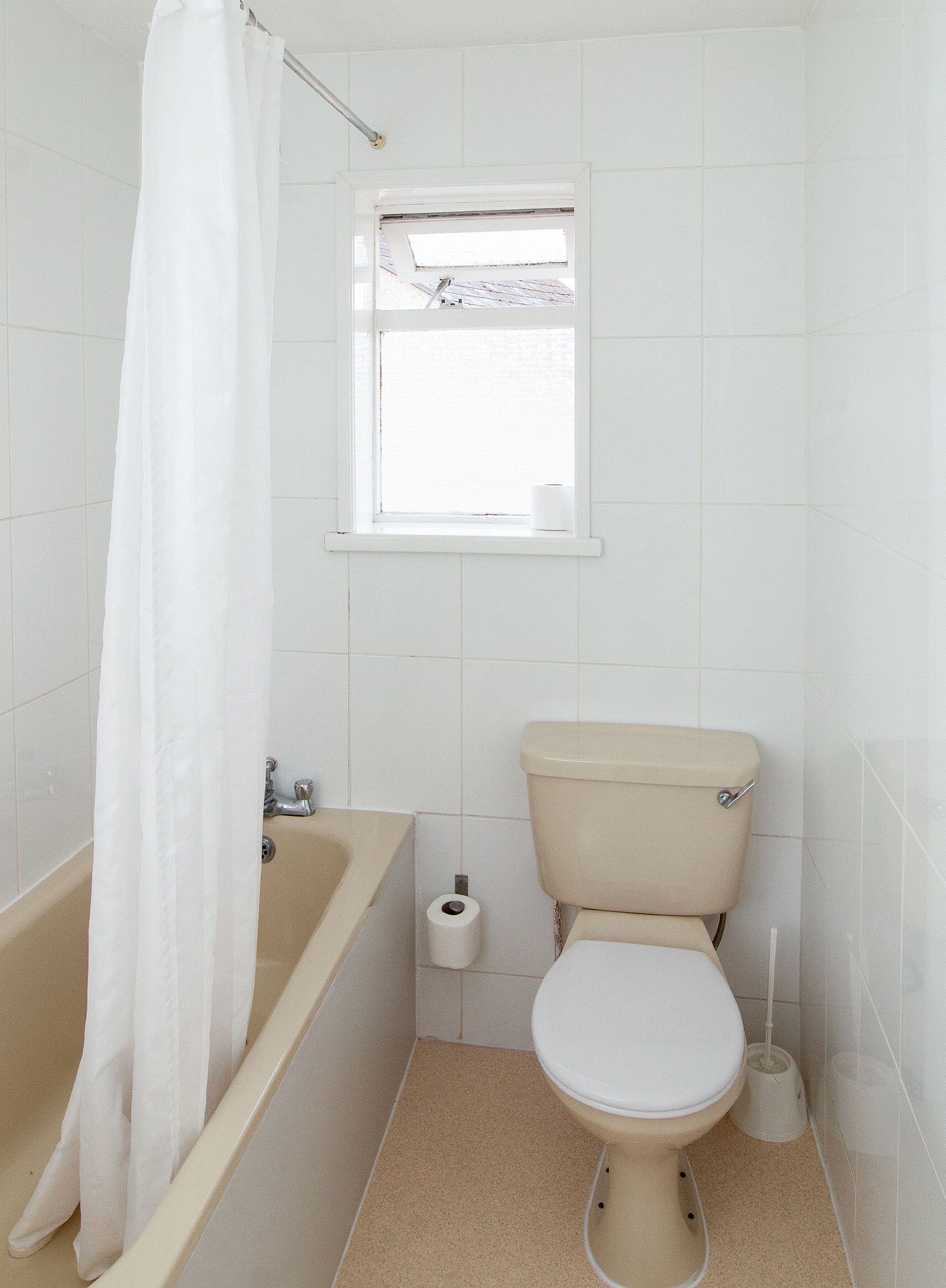 A small, white bathroom with a bathtub, toilet, and a window above the toilet.