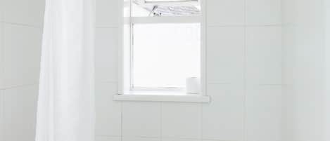 Une petite salle de bain blanche, avec une baignoire, des toilettes et une fenêtre située au-dessus des toilettes.