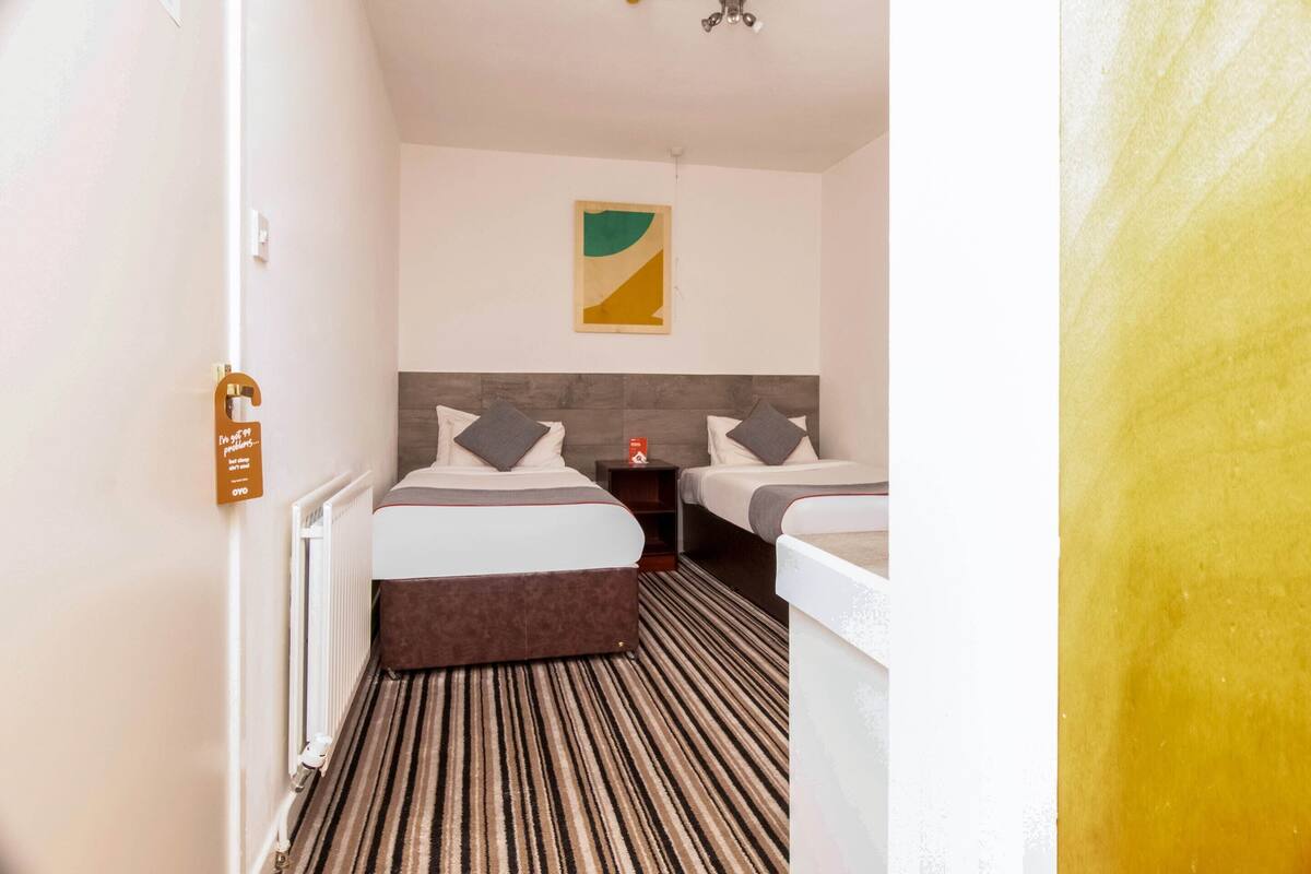 A hotel room with two beds, a striped carpet, a modern headboard, and a wall-mounted artwork.
